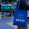 Person carrying a royal blue custom tote bag printed with a Nexus Tech Summit logo at a trade show.