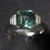 Emerald Cut Teal Sapphire Ring with baguette diamond sides against dark background