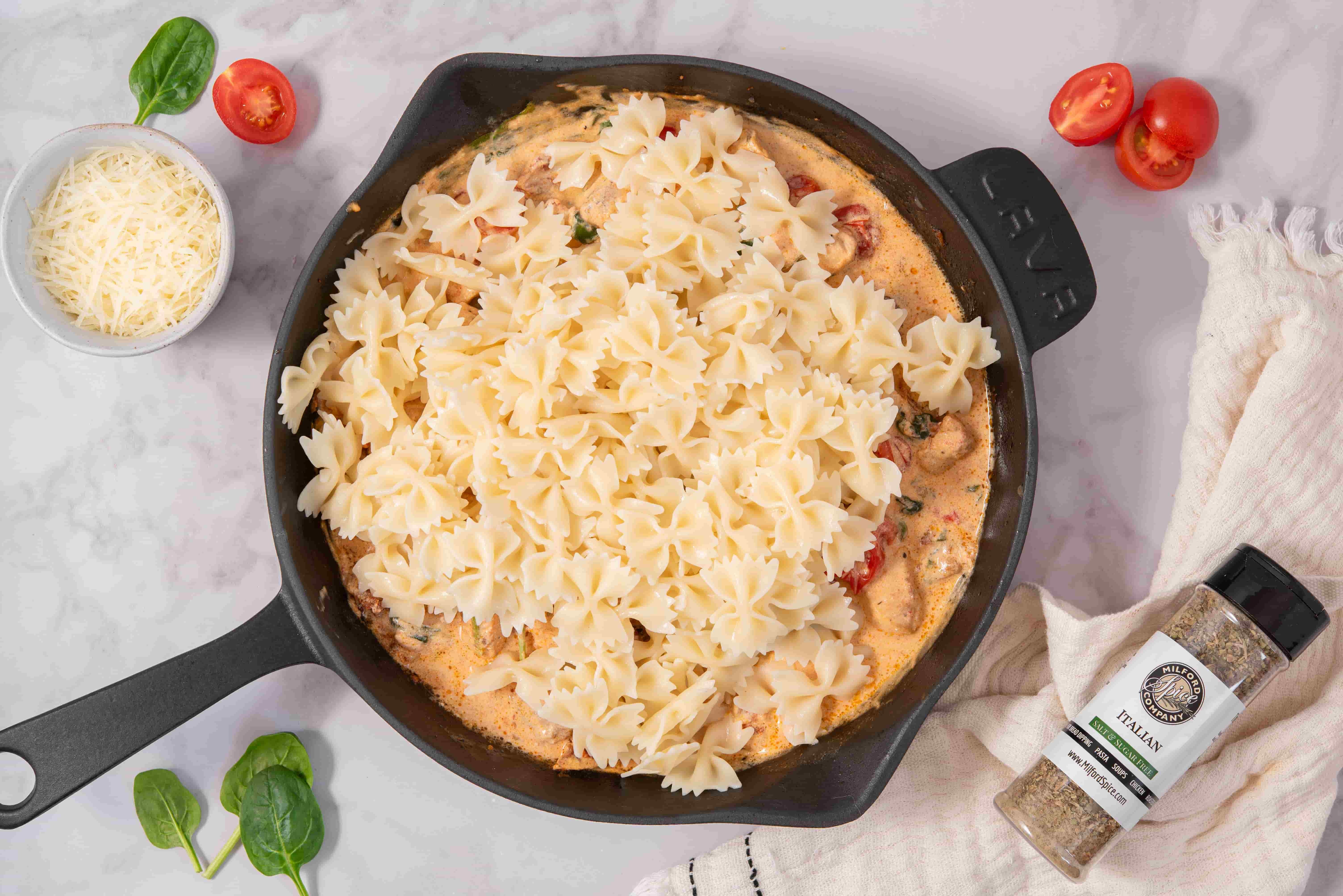 Bow tie pasta added to creamy Marry Me Chicken sauce in a skillet with Milford Salt Free Italian Seasoning nearby