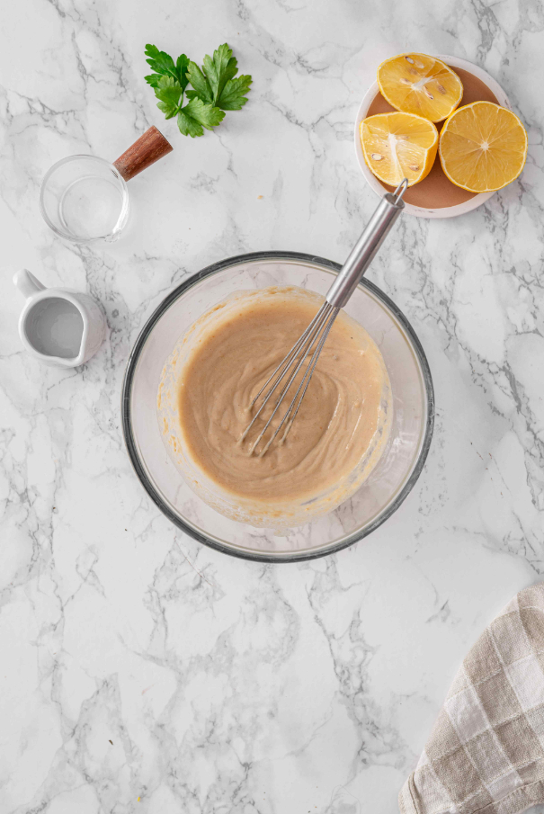 Creamy lemon tahini sauce whisked smooth in a glass bowl