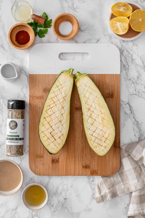 Eggplant halves scored on a cutting board with lemon, parsley, olive oil, smoked paprika, tahini, and Milford Spice Company Salt Free Italian