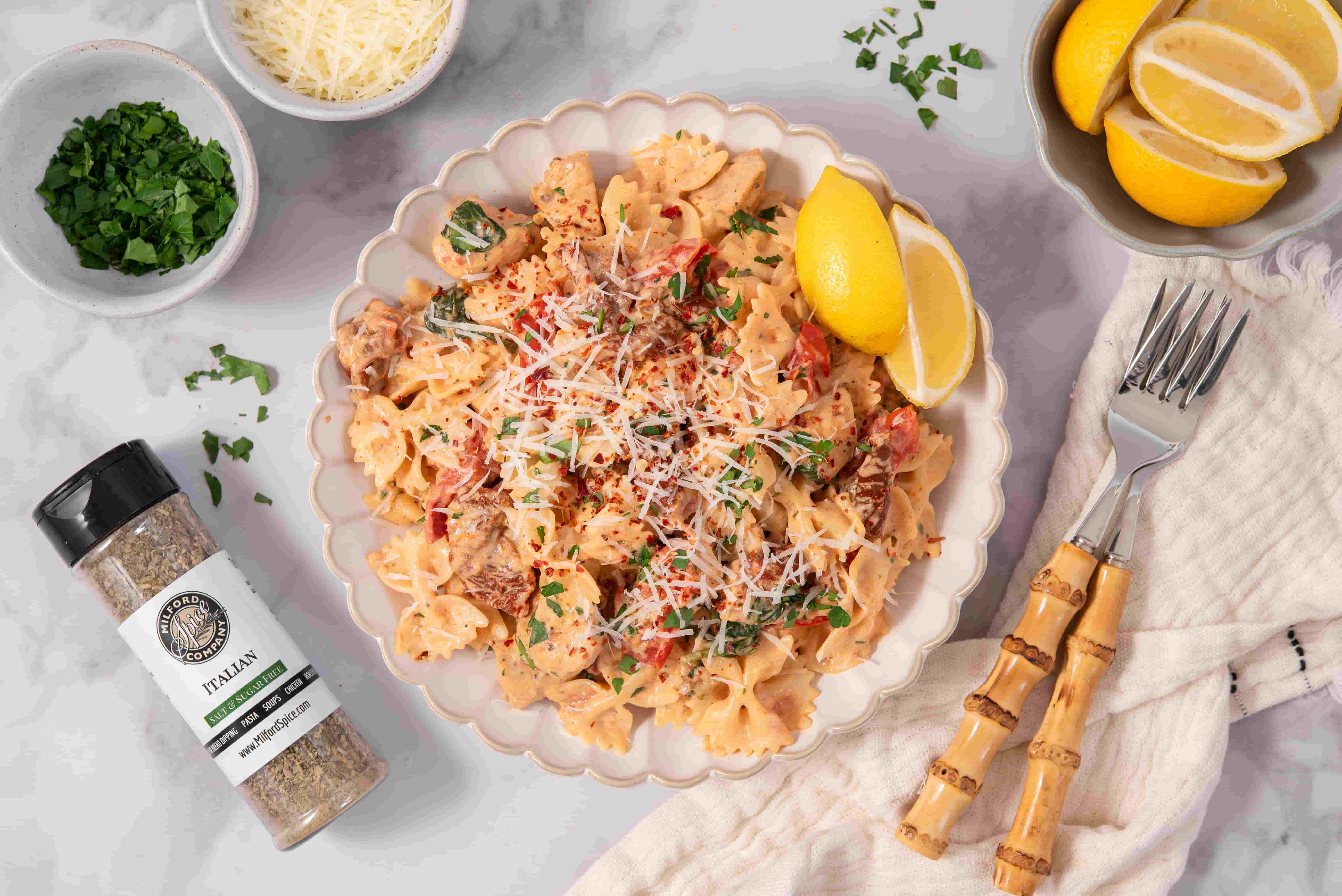 Marry Me Chicken Pasta with bow tie pasta, creamy sauce, chicken, spinach, tomatoes, Parmesan, lemon wedges, and Milford Spice Company Salt Free Italian Seasoning