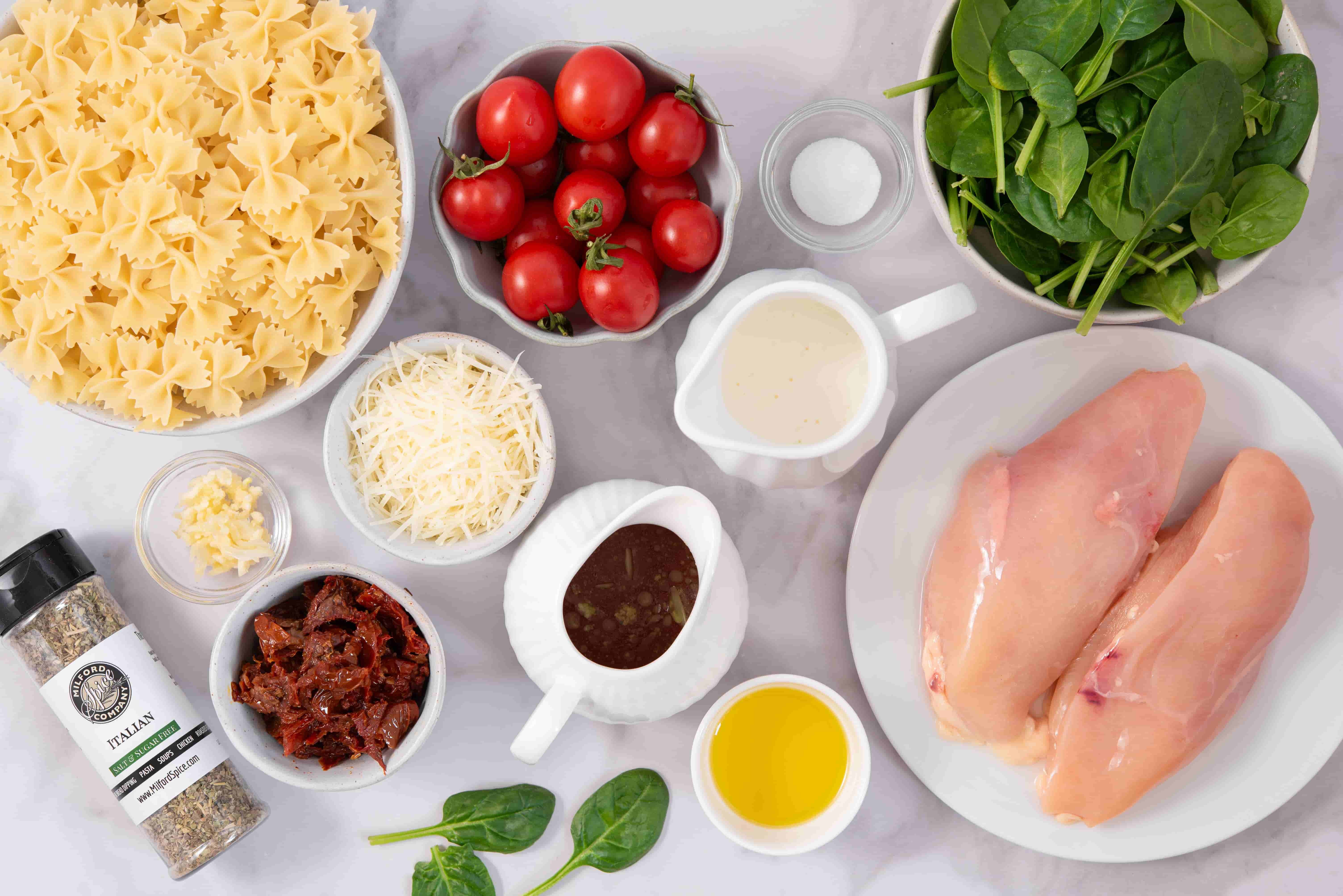 Ingredients for Marry Me Chicken Pasta including bow tie pasta, chicken breasts, cherry tomatoes, sun-dried tomatoes, spinach, cream, Parmesan, garlic, olive oil, and Milford Salt Free Italian Seasoning