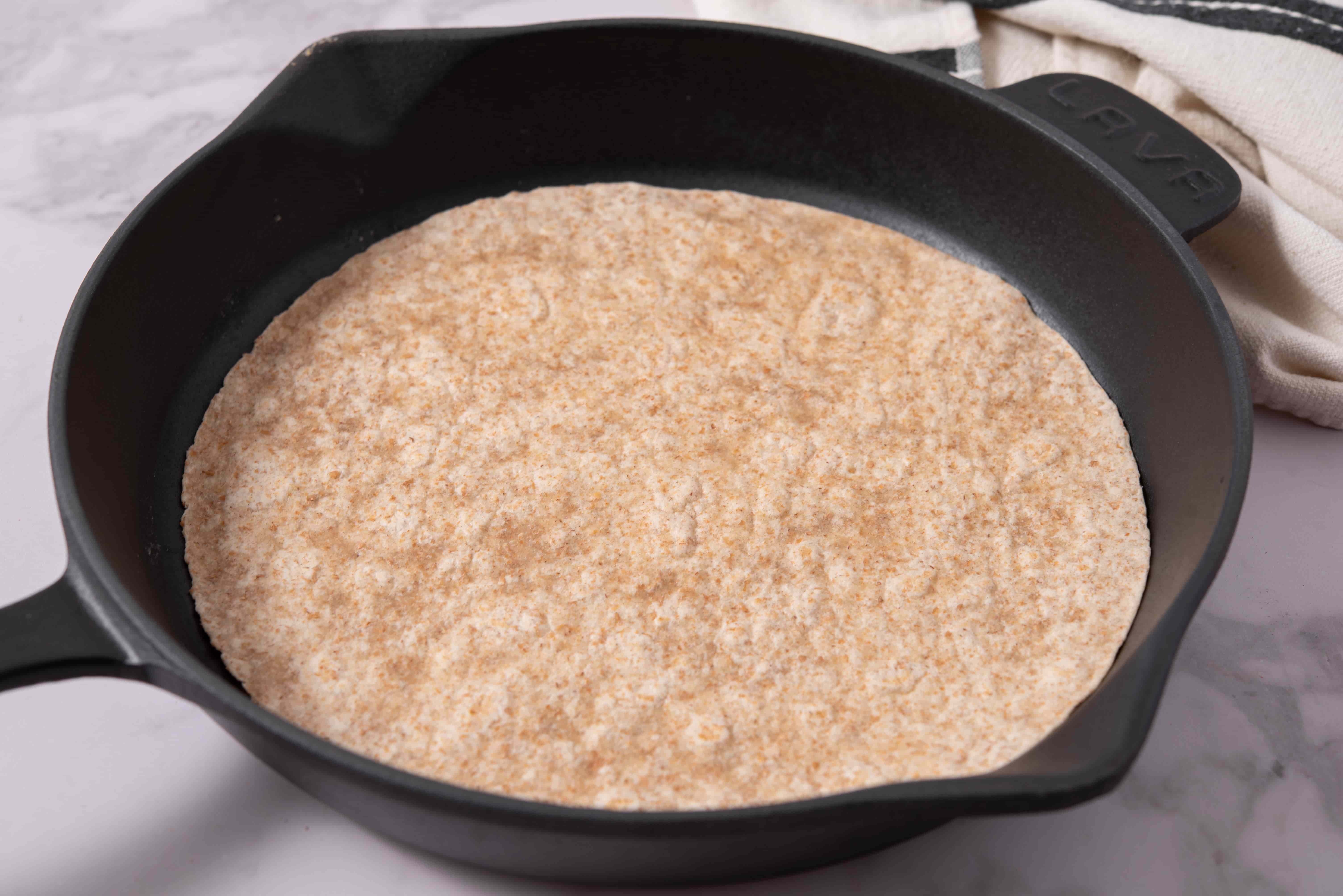 Whole-wheat tortilla warming in a cast iron skillet for BBQ Chicken Tortilla Folds