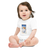 Baby in a white, short sleeve baby onesie featuring an illustration of a yellow lab puppy sitting in a ski chair lift