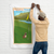 Man hanging a wall flag illustrated with a tan Frenchie sitting on a golf course