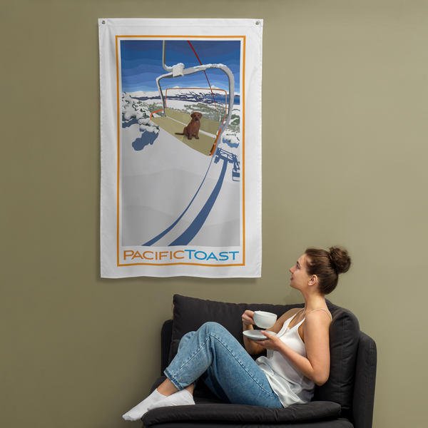 A sitting woman drinks coffee while admiring a wall banner illustrated with a cute, chocolate Labrador puppy on a ski chair lift