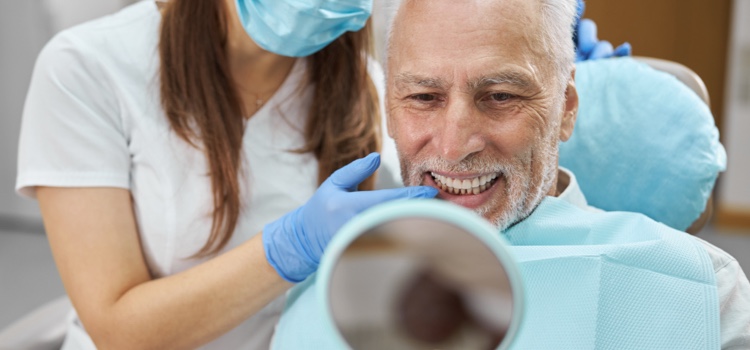 Male dental patient smiling into a handheld mirror after care.