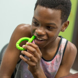 A child chews the lime green Textured Grabber®  Sensory Chew; a P-shaped chew with a long extension to reach the back molars.