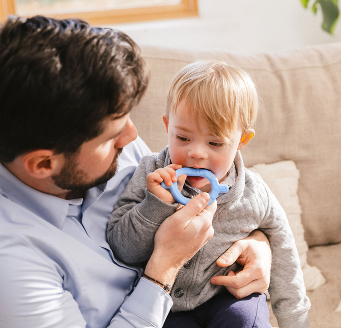 A father guides baby in mouthing the Baby Grabber; a combo textured and smooth baby chew great for sensory exploration