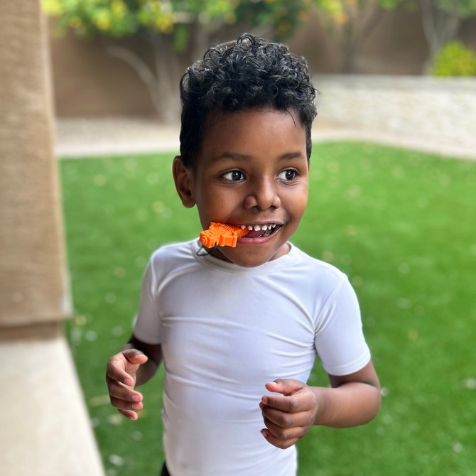A child chews an orange RoboChew, a chew with diverse texture perfect as a replacement for chewing on toys
