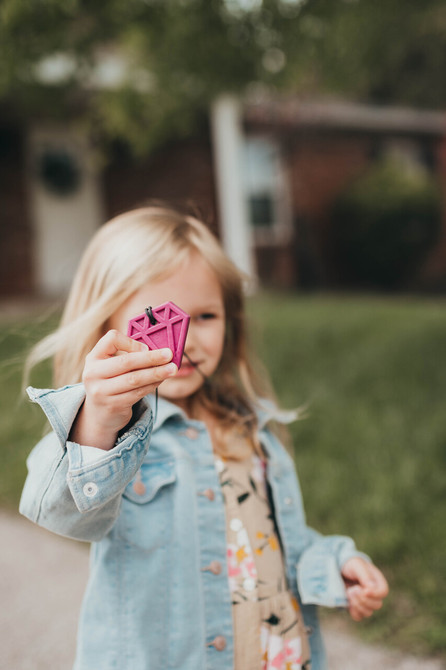 A young girl shows off her chewable Diamond necklace, a wide shape with mild texture, best for front teeth and premolar chewing