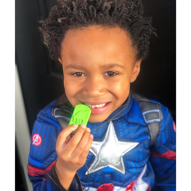 A child dressed for Halloween chews a lime green BOO Chew® Ghost Necklace;  a robust dog tag shape great for avid chewers.