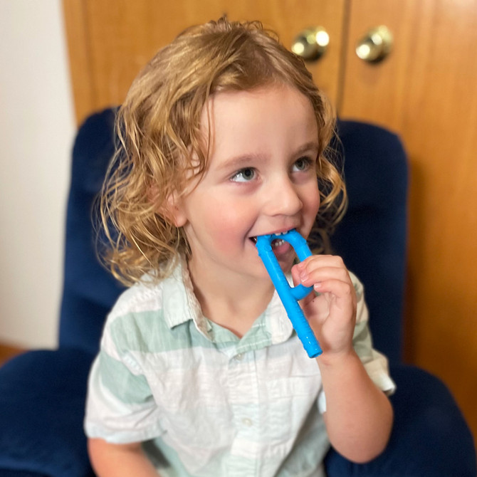 A child chews a bright blue Textured Grabber® P Tube (Hollow Chew Tool); a textured chew with a loop handle and hollow stem