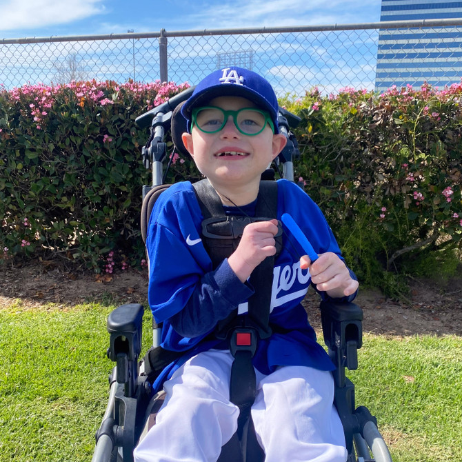 A child holds a royal blue Baseball chew necklace; a long/slender shape perfect for back molar chewing