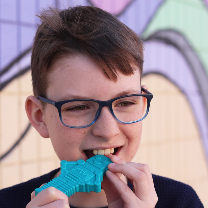 A child chews a teal MEGA RoboChew™ Robot Chewy; a large, heavily textured robot-shaped chew
