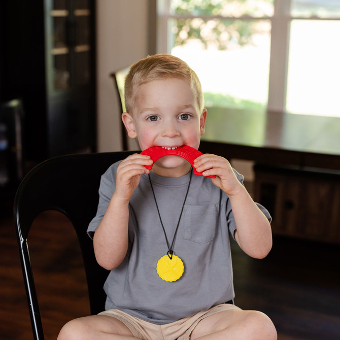 A young boy bites the Red, Softest Chewable Rainbow Fidget - best suited for mild chewers.