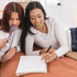 A young woman chews a Lime Green Chewlinder, a thin, hollow chew tool, while doing homework with a friend