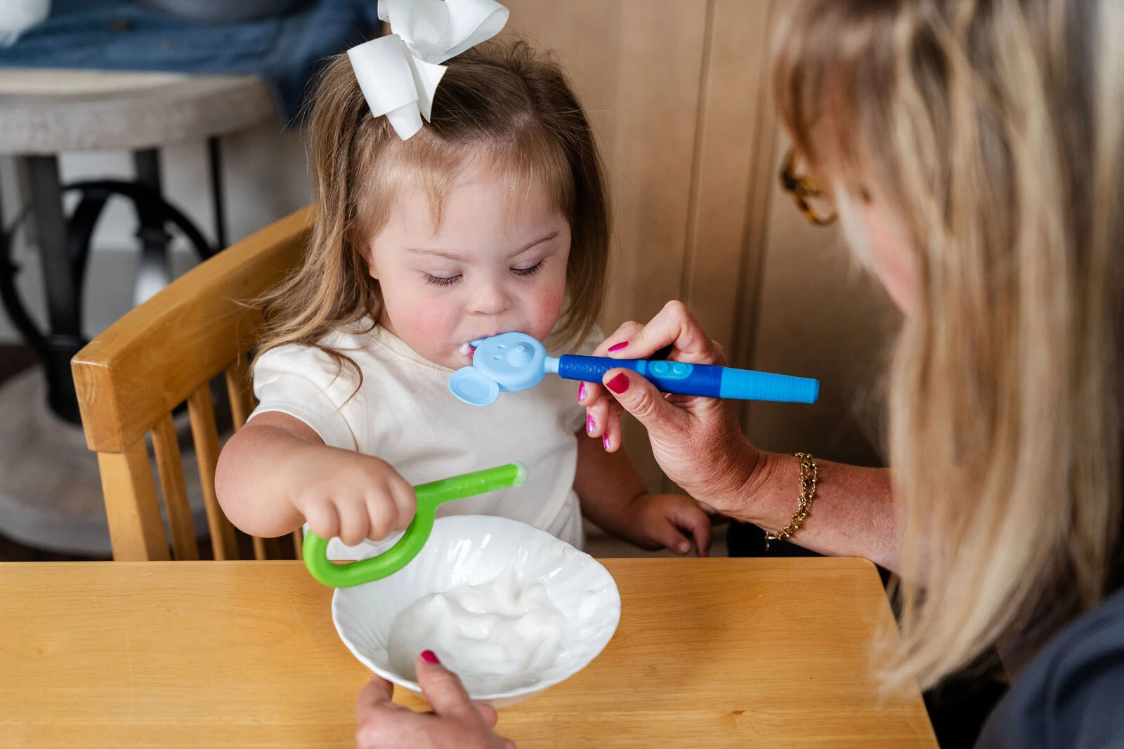 A caregiver uses a Z-Vibe Plus spoon tip to help a young girl at mealtime as she reaches for her own utensil.