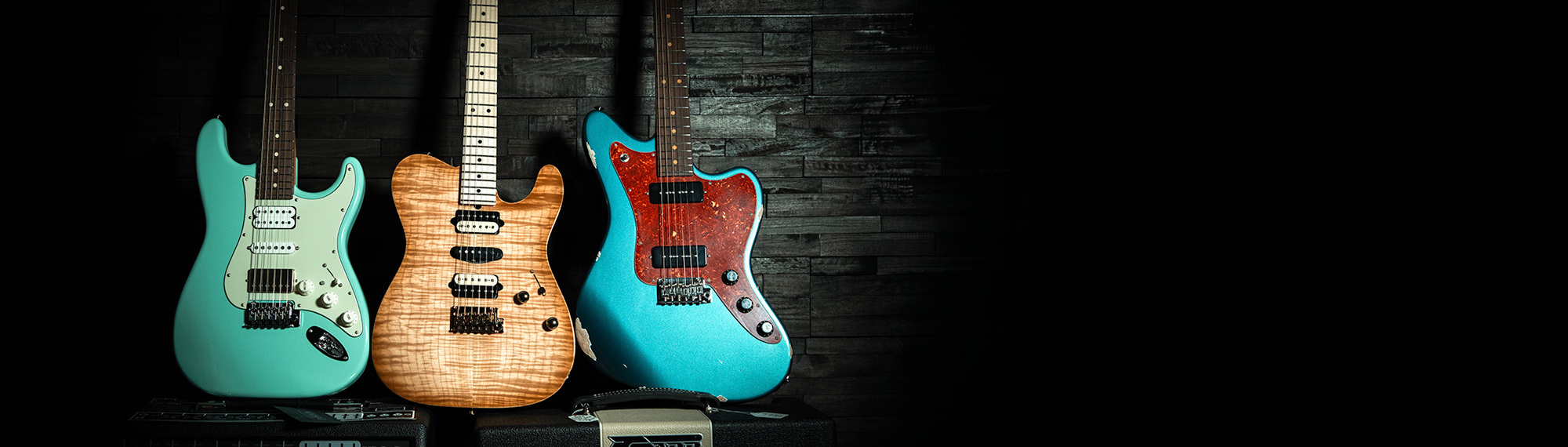 Three Suhr Guitars Leaning Against a Dark Wood Wall