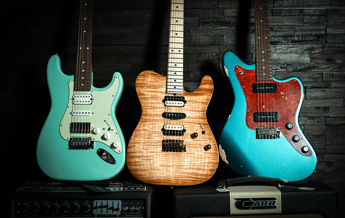 Three Suhr Guitars Leaning Against a Dark Wood Wall
