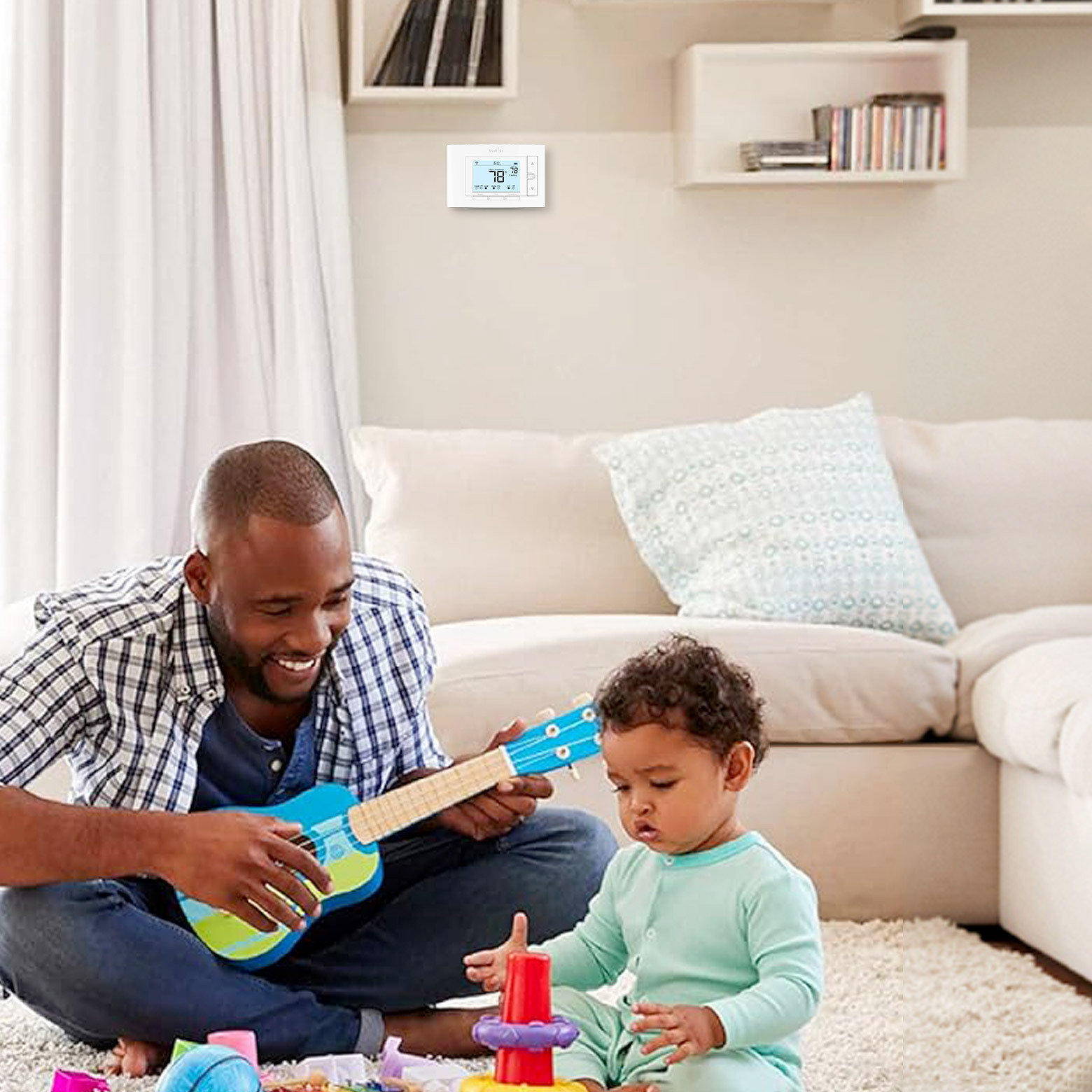 Father and son playing on the living room floor with the Sensi thermostat on the wall in the background