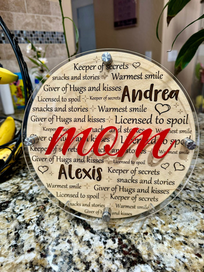 Custom-engraved circular wooden plaque with names Andrea and Alexis prominently displayed amongst heartfelt phrases like 'Keeper of secrets' and 'Giver of hugs and kisses