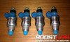 Four top feed fuel injectors, front view, blue bodies, green O-rings, silver metal bases with fittings