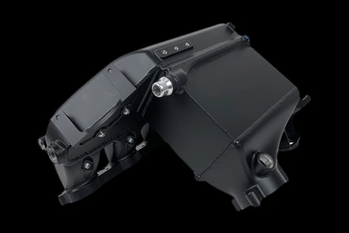 CSF S58 charge air cooler manifold in black, angled view showing bolt bosses and inlet fitting