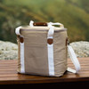 A tan canvas cooler bag with white straps and a brown handle, featuring a side pocket.