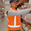 An orange reversible fleece lined safety vest with reflective strips, worn by a person in a warehouse setting.