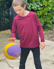 A burgundy longsleeve shirt worn by a child playing with a purple and yellow basketball outdoors.