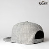 A grey snapback cap with a textured finish, featuring a logo and an adjustable strap at the back.