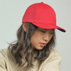 A red cap with a curved brim, featuring a logo, worn by a person with wavy hair, set against a light background.