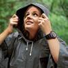 A woman wearing a grey rain poncho with a hood, looking upwards in a natural setting.