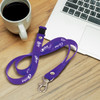 A purple silicone lanyard with a clip, placed on a wooden surface near a coffee cup and a laptop.