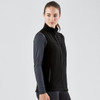 A black softshell vest with a zip front, worn over a long-sleeve top. It features a side pocket and has a logo.