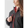 A woman models a black and red insulated softshell jacket with a zipper and hood. The jacket has a subtle logo.
