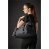 A black duffle bag is worn over the shoulder by a model dressed in black activewear. The bag features a logo.
