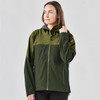 A woman models a green and dark green Women's Vertex Stormshell jacket with a hood. The jacket features a logo.