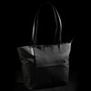 A black tote bag with leather handles and a front pocket, featuring a logo on the side.