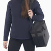 A cooler bag with a grey and black design being held by a person wearing a navy sweater. The bag has a strap and a handle.