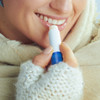 A lip balm with a blue cap is being applied to a person's lips. The individual is wearing a cozy sweater and a scarf.