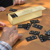 A wooden box containing black dominoes scattered on a table, with hands visible playing the game.