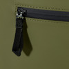 A close-up of a dark olive green roll-top backpack featuring a zippered pocket and a black zipper pull.