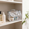 A transparent waterproof cosmetic bag in silver, filled with various skincare products, sits on a shelf.