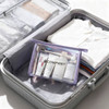 A clear, purple travel cosmetic bag filled with toiletries, placed inside a suitcase alongside folded clothes.