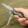 A multi-tool in a hand featuring a knife, a serrated blade, and pliers. The tool has a grey body.
