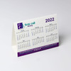 A desk calendar featuring months from January to June 2022, with a white background and purple accents. It includes a logo.