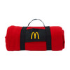 A rolled red blanket secured with a black strap featuring a logo. The blanket is compact and portable.